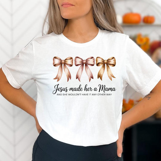 A woman wearing a white t-shirt with a graphic design of three bows and text that reads "Jesus made her a Mama and she wouldn't have it any other way".