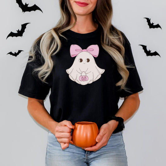 A woman wearing a black t-shirt with a cartoon ghost and a pink bow, holding a pumpkin-shaped mug.