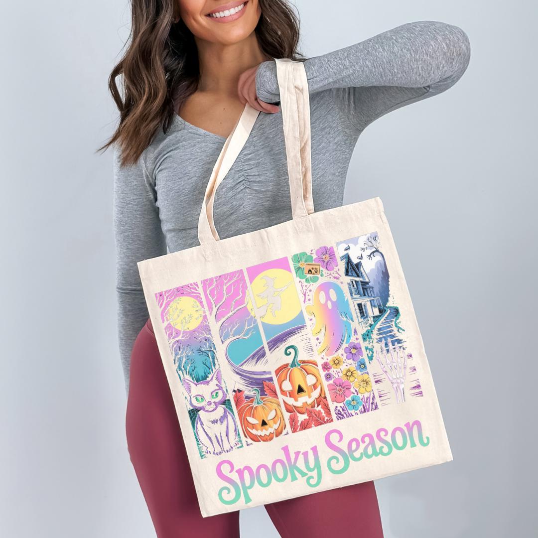 A woman is holding a large tote bag with a Halloween-themed design, including a cat, pumpkin, ghost, and castle.