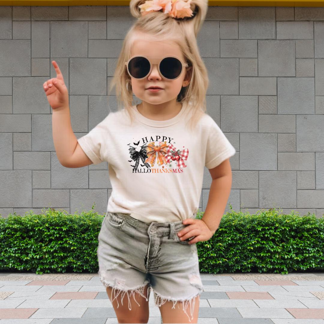 A young girl wearing a white t-shirt with a graphic design, sunglasses, and denim shorts is standing in front of a brick wall.