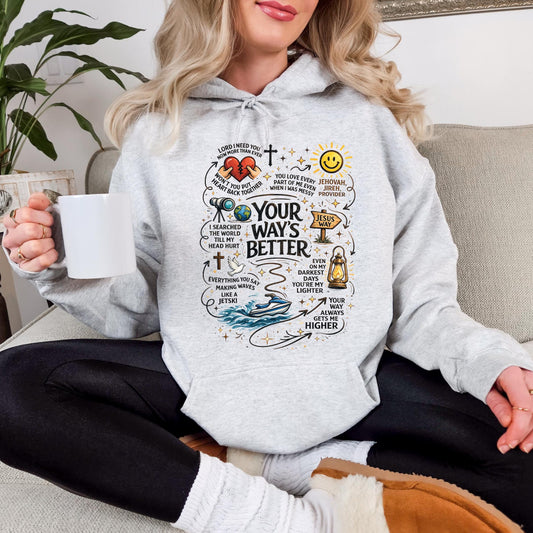 A woman wearing a grey hoodie with a colorful graphic design on it, sitting on a couch and holding a coffee mug.