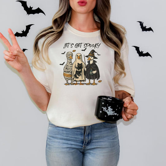 A woman wearing a white t-shirt with a Halloween-themed graphic and holding a black mug with a Halloween-themed design.