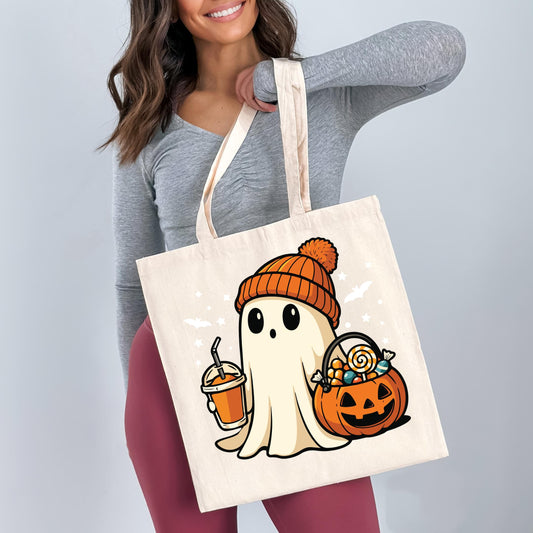 A woman is holding a white tote bag with a Halloween-themed graphic of a ghost wearing a hat and holding a pumpkin and a drink.
