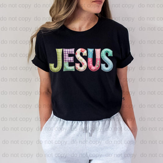 A woman wearing a black t-shirt with the word "JESUS" printed in colorful letters.