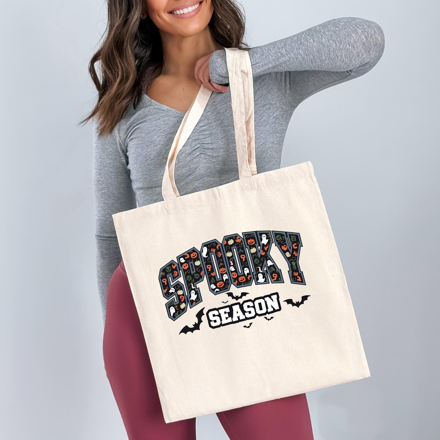 A woman is holding a white tote bag with the text "SPOOKY SEASON" printed on it.