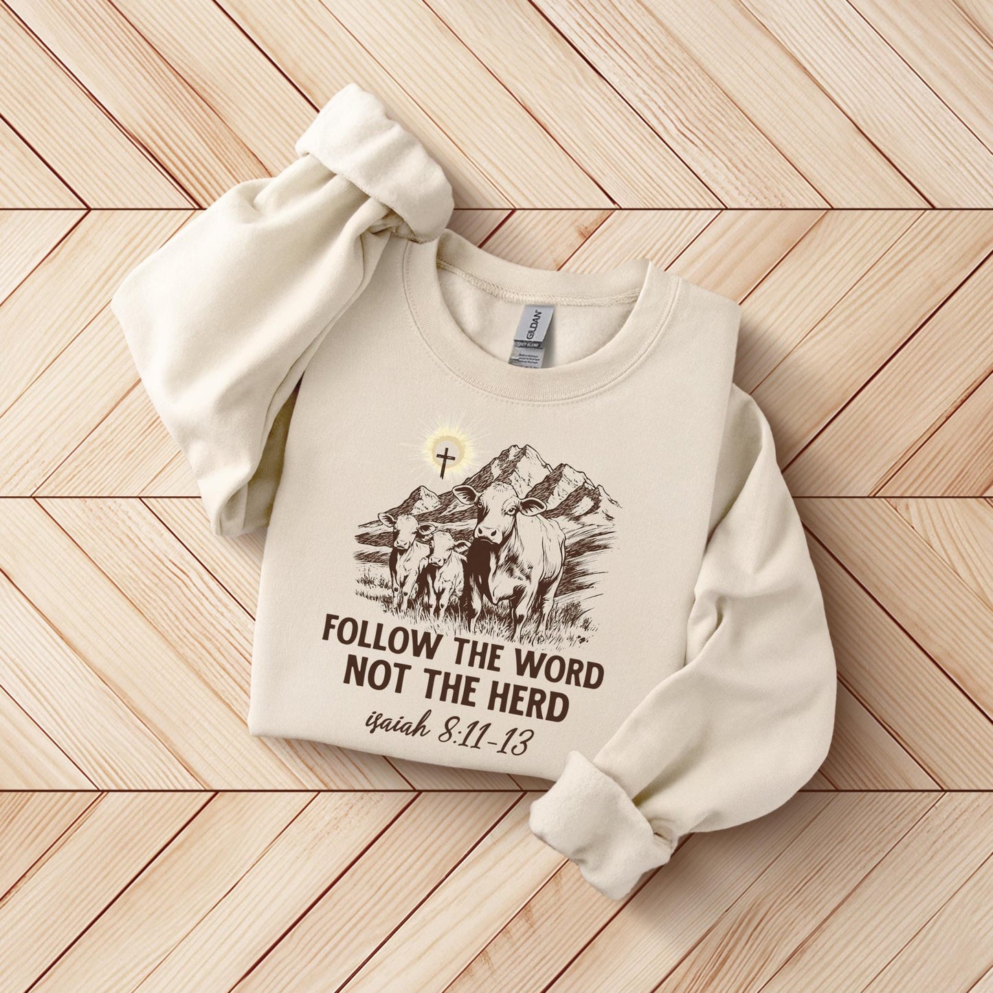 A beige sweater with a graphic design and text printed on it, laid out on a wooden surface.