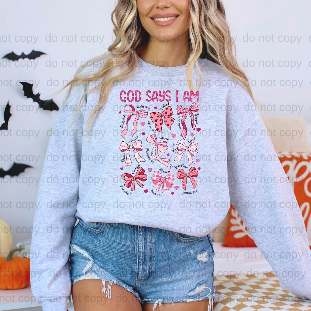 A woman wearing a gray sweatshirt with a graphic design of pink bows and hearts, standing in front of a wall with bats.