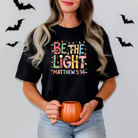 A woman wearing a black t-shirt with a colorful design and holding a pumpkin-shaped mug.