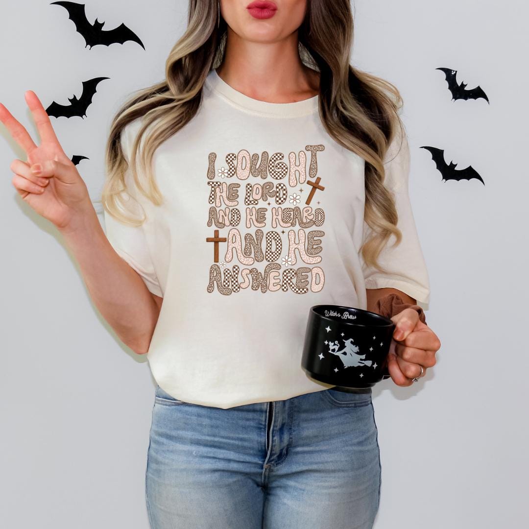 A woman wearing a white t-shirt with a text design and holding a black mug with a star and bat pattern.