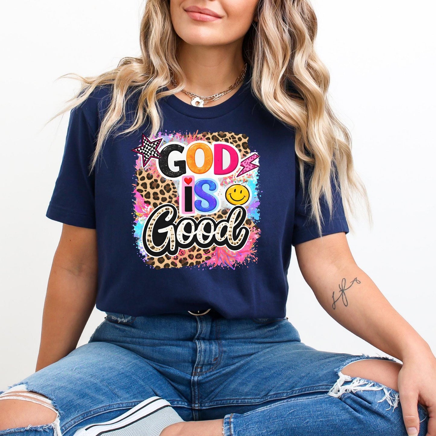 A woman wearing a navy blue t-shirt with a colorful graphic design and text, sitting on the floor with her legs crossed.