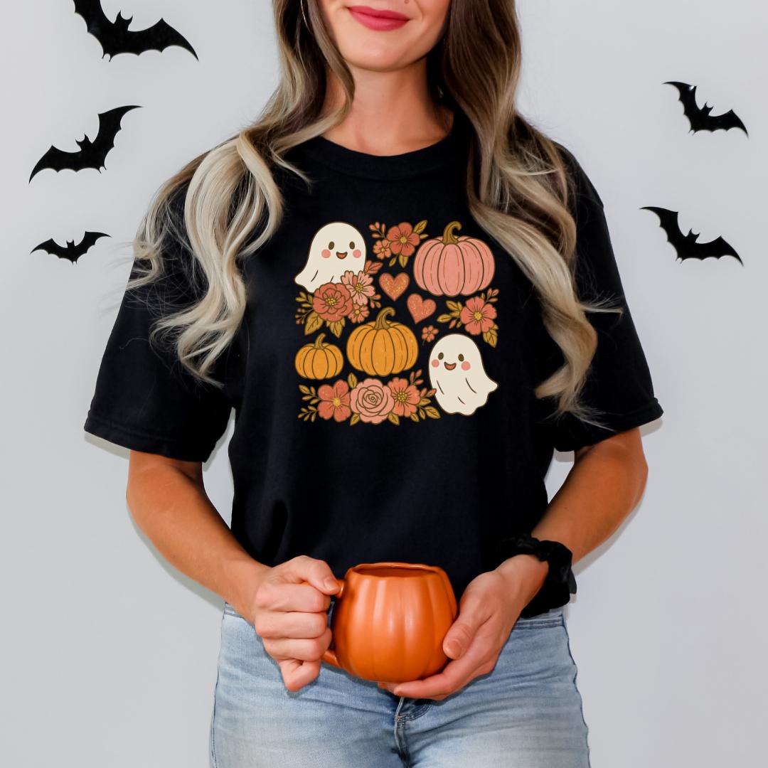 A woman wearing a black t-shirt with a graphic design of Halloween-themed pumpkins and ghostly figures holding a pumpkin.