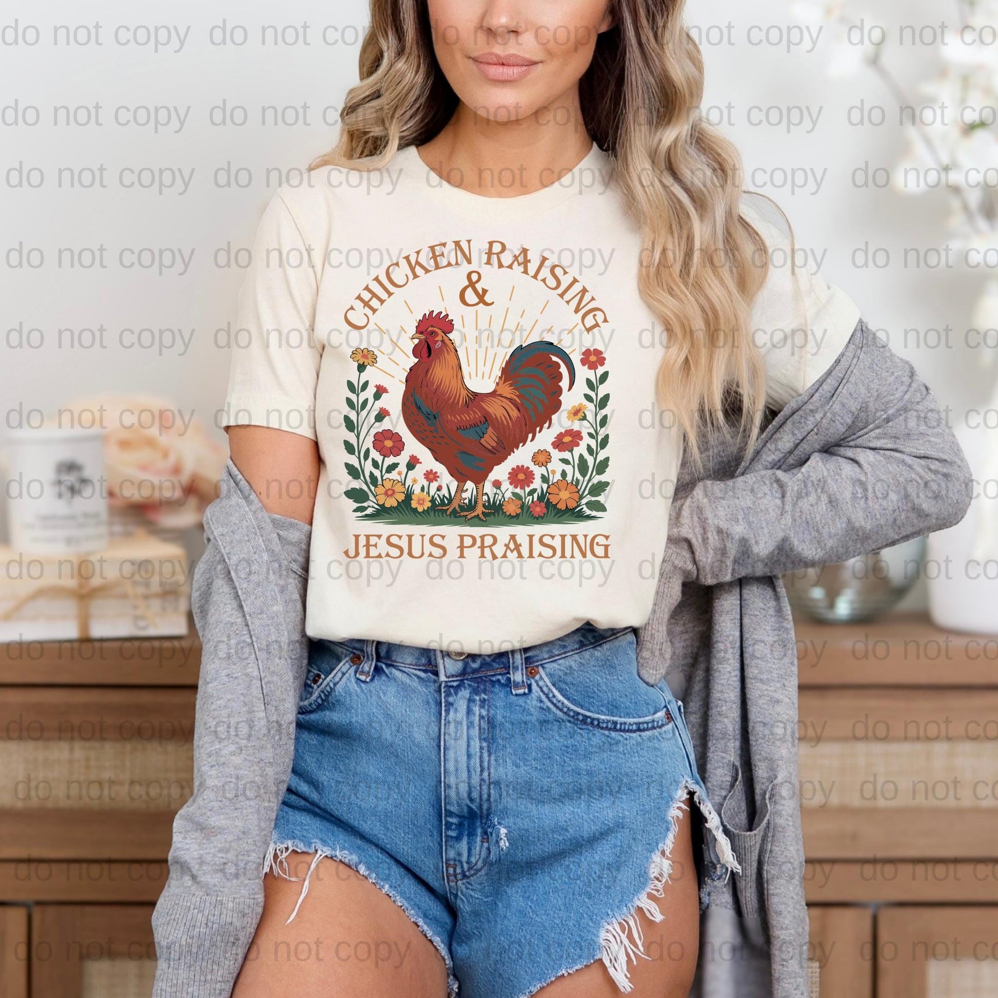 A woman wearing a white t-shirt with a graphic of a rooster and the text "Chicken Raising & Jesus Praising" is standing in front of a wooden cabinet.