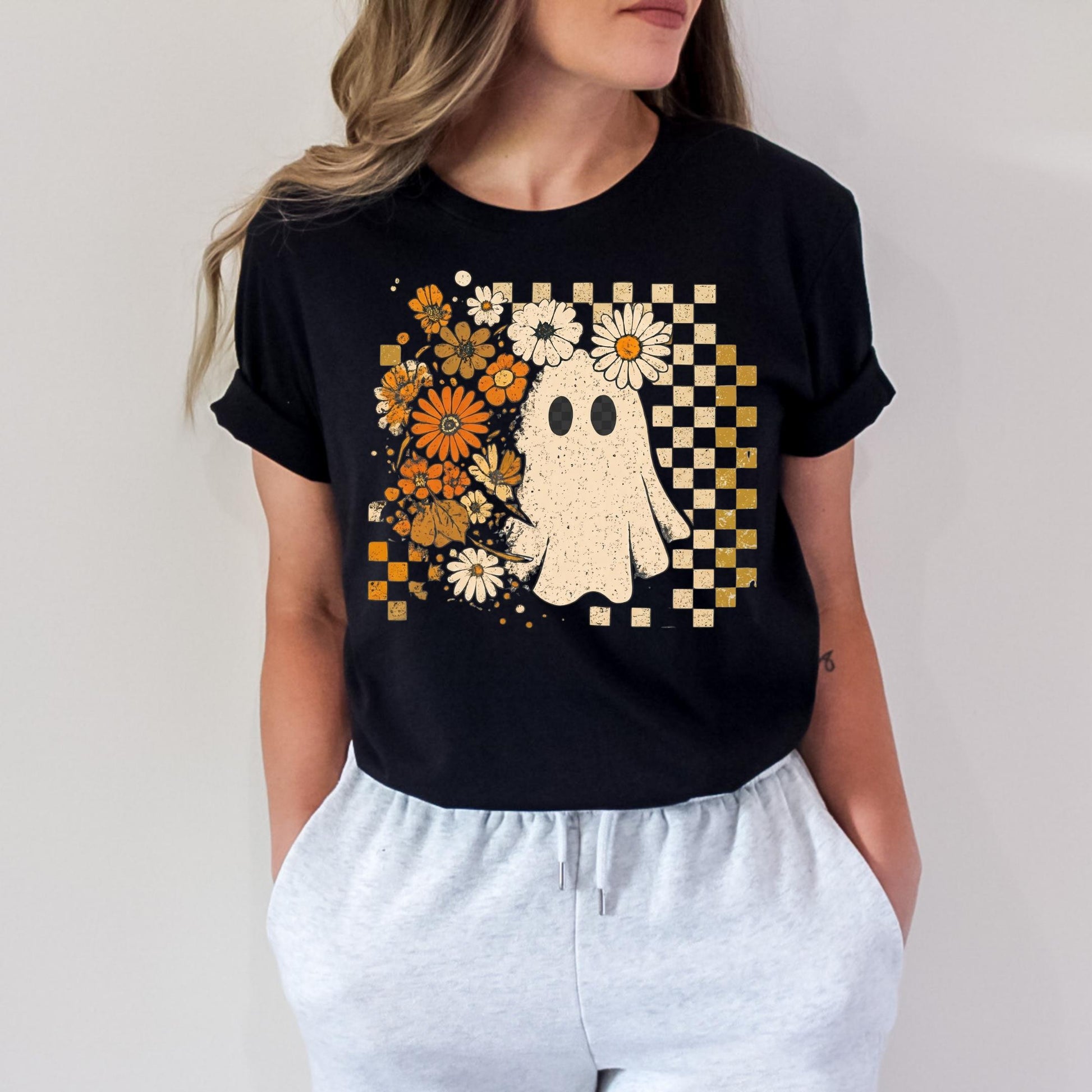 A woman wearing a black t-shirt with a graphic design of a ghost surrounded by flowers and a checkered pattern.