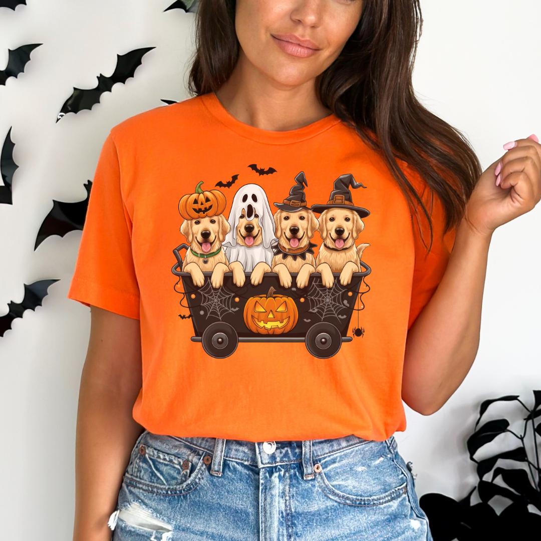 A woman wearing an orange t-shirt with a graphic of four dogs in a wagon, including a ghost and a witch, along with a jack-o-lantern.