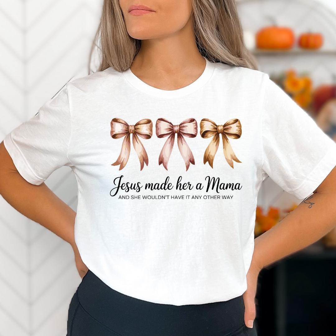 A woman wearing a white t-shirt with a graphic design of three bows and text that reads "Jesus made her a Mama and she wouldn't have it any other way".