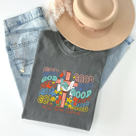 A gray t-shirt with a colorful graphic design, a pair of blue jeans, and a beige hat are arranged on a white surface.