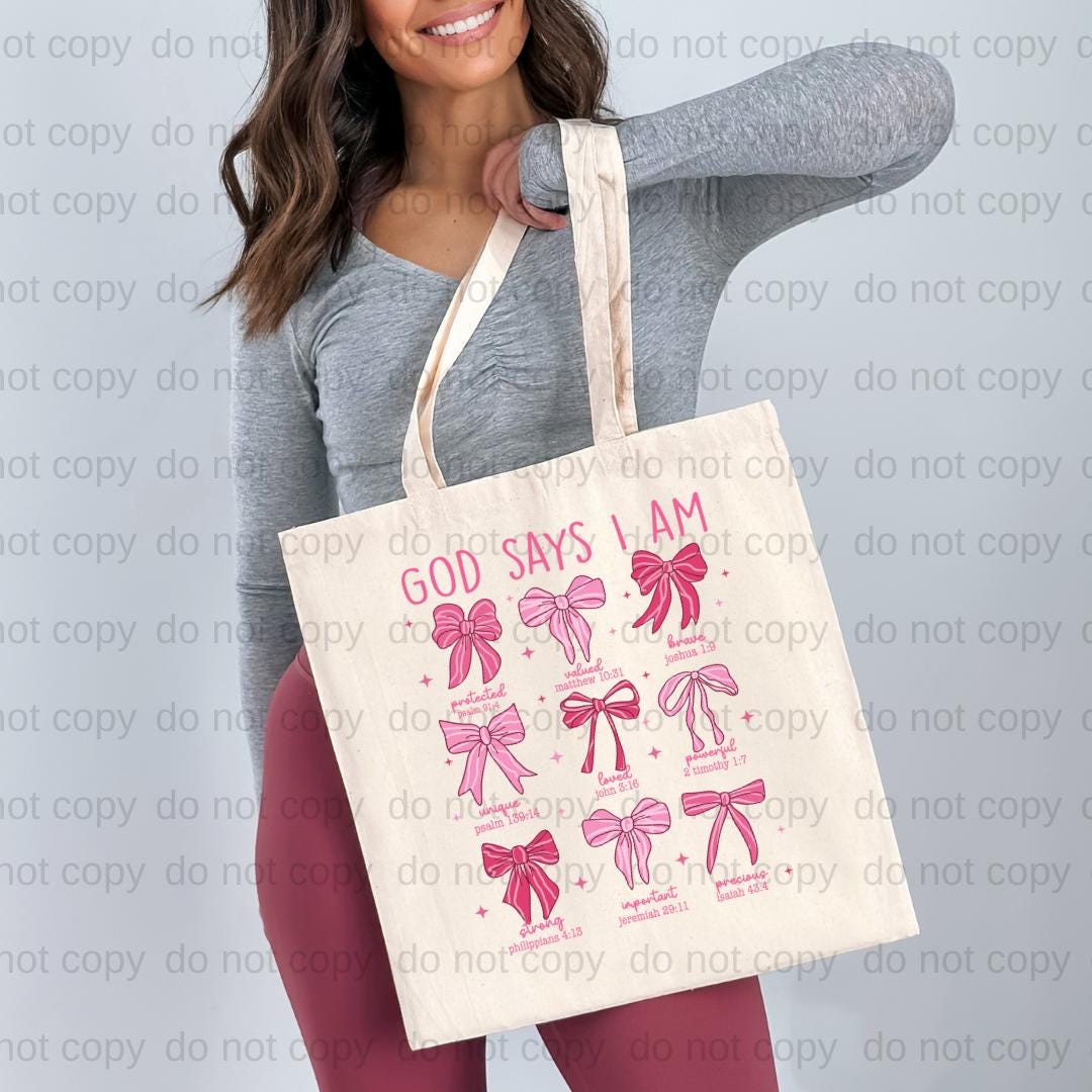 A woman is holding a white tote bag with pink bows and text on it.