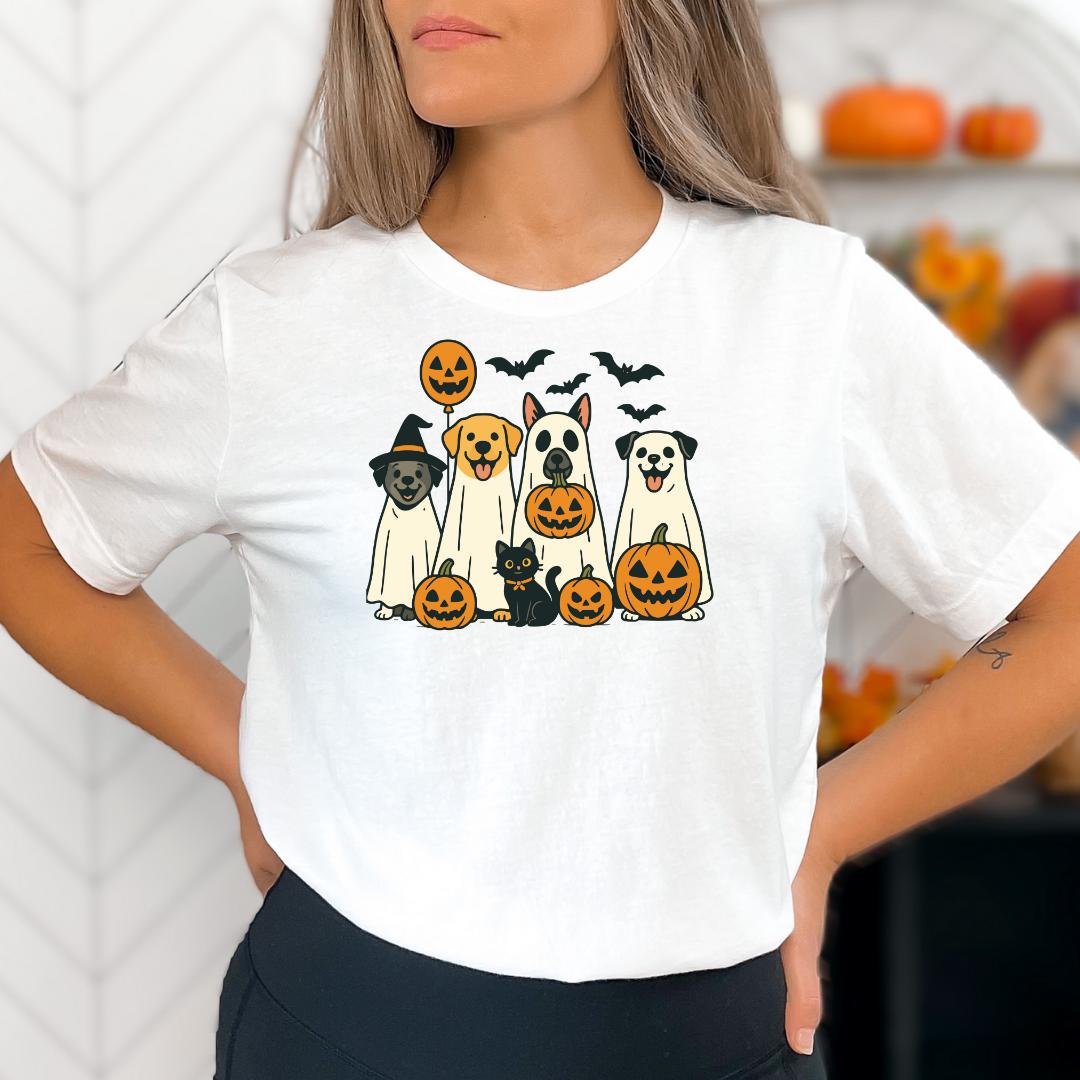 A woman wearing a white t-shirt with a graphic design of a group of dogs and cats, including a witch, a dog, a cat, and a pumpkin.