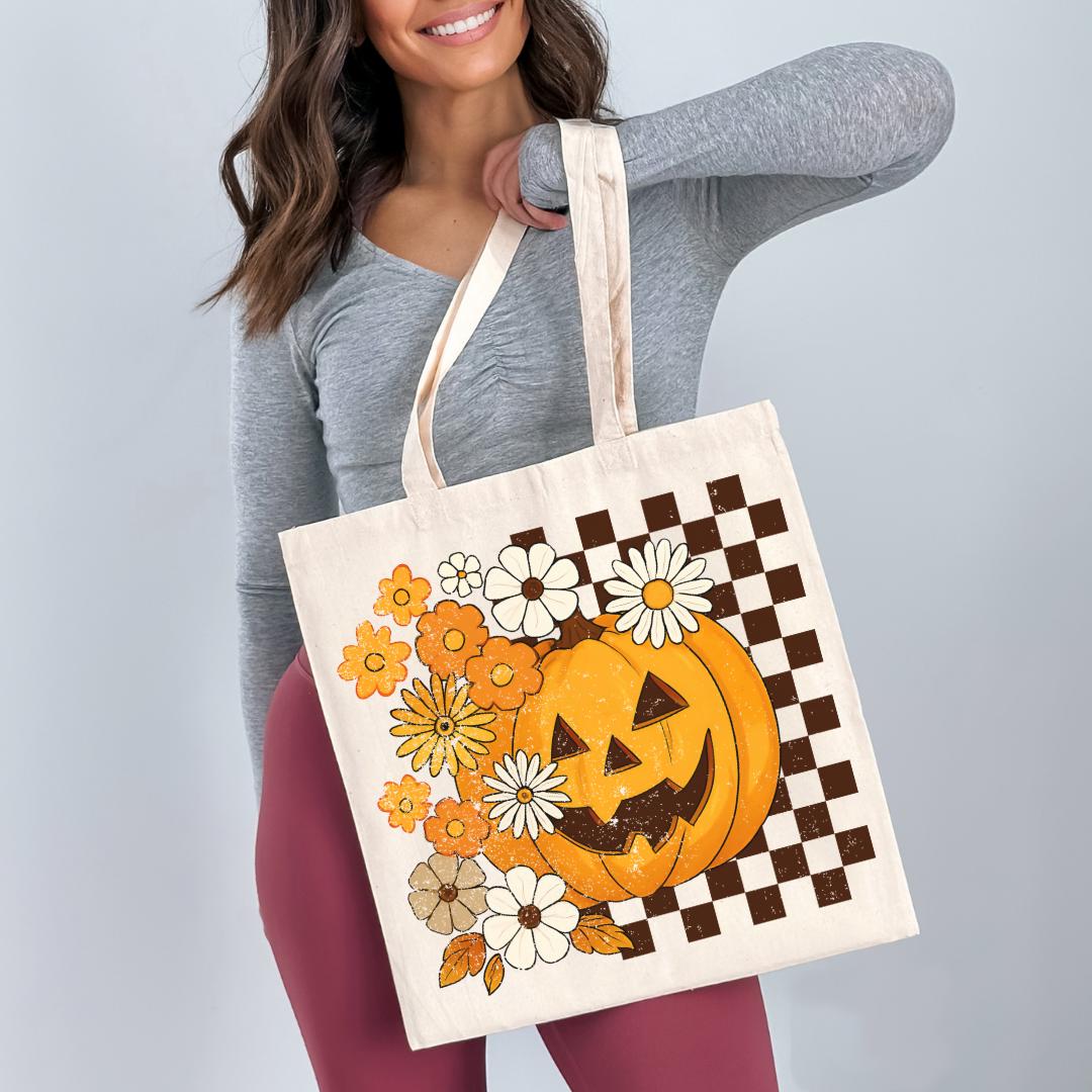 A woman is holding a large tote bag with a pumpkin and flower design on it.