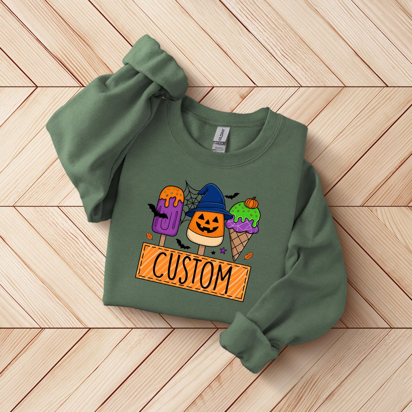 A green sweatshirt with a Halloween-themed graphic design, including a pumpkin, spider, and ice cream cones, along with the word "CUSTOM" printed on it.