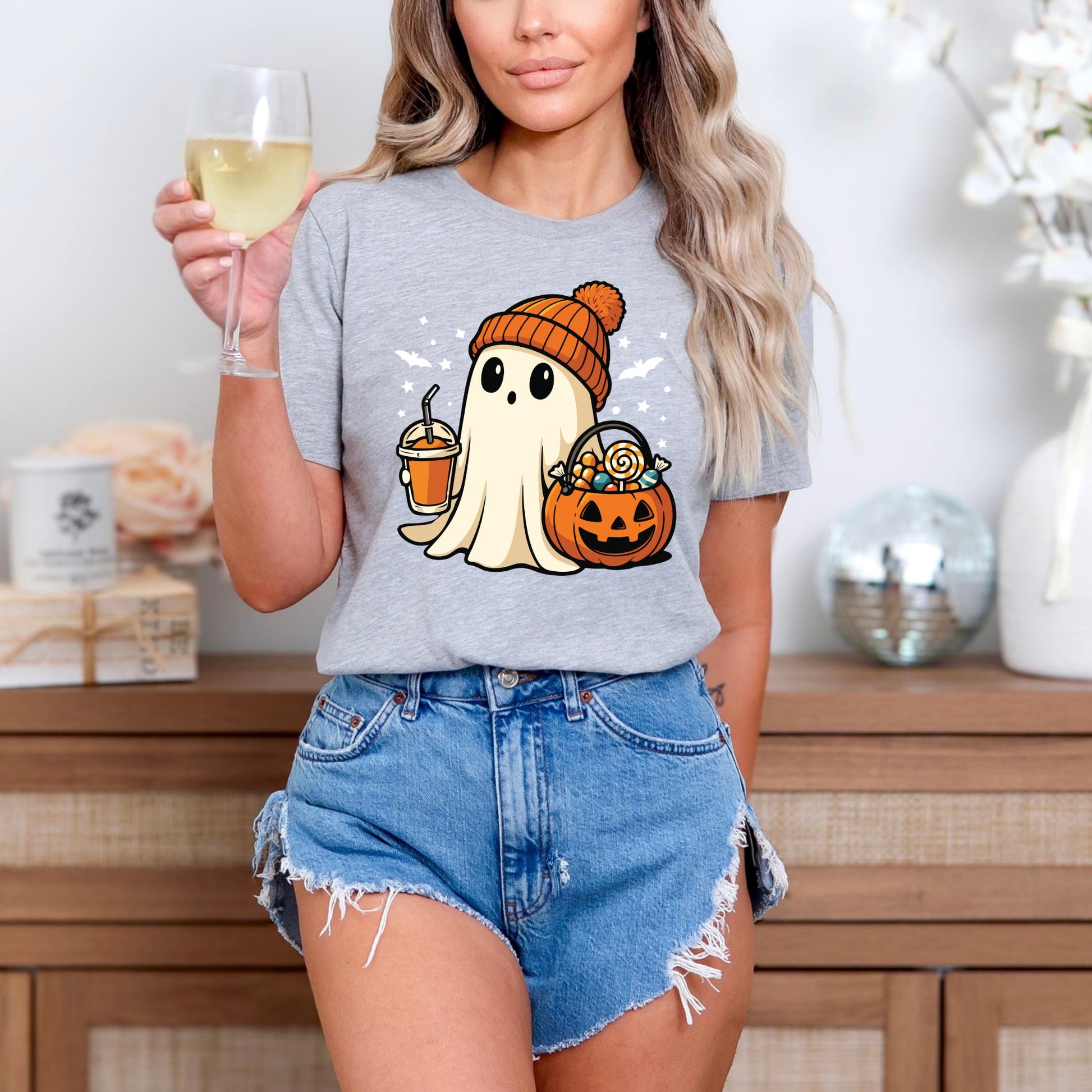 A woman wearing a gray t-shirt with a ghost graphic and denim shorts is holding a glass of wine.
