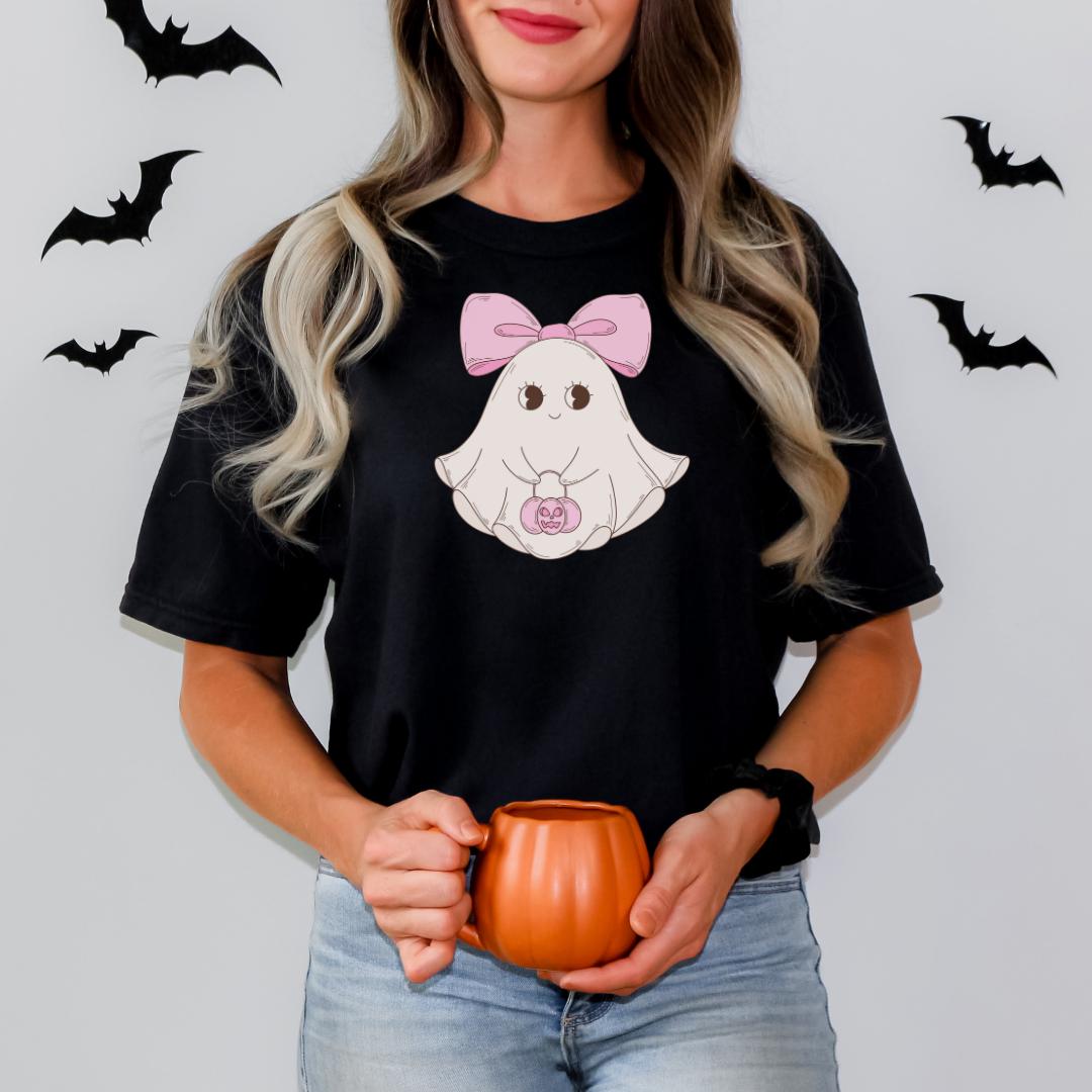 A woman wearing a black t-shirt with a cartoon ghost and a pink bow, holding a pumpkin-shaped mug.
