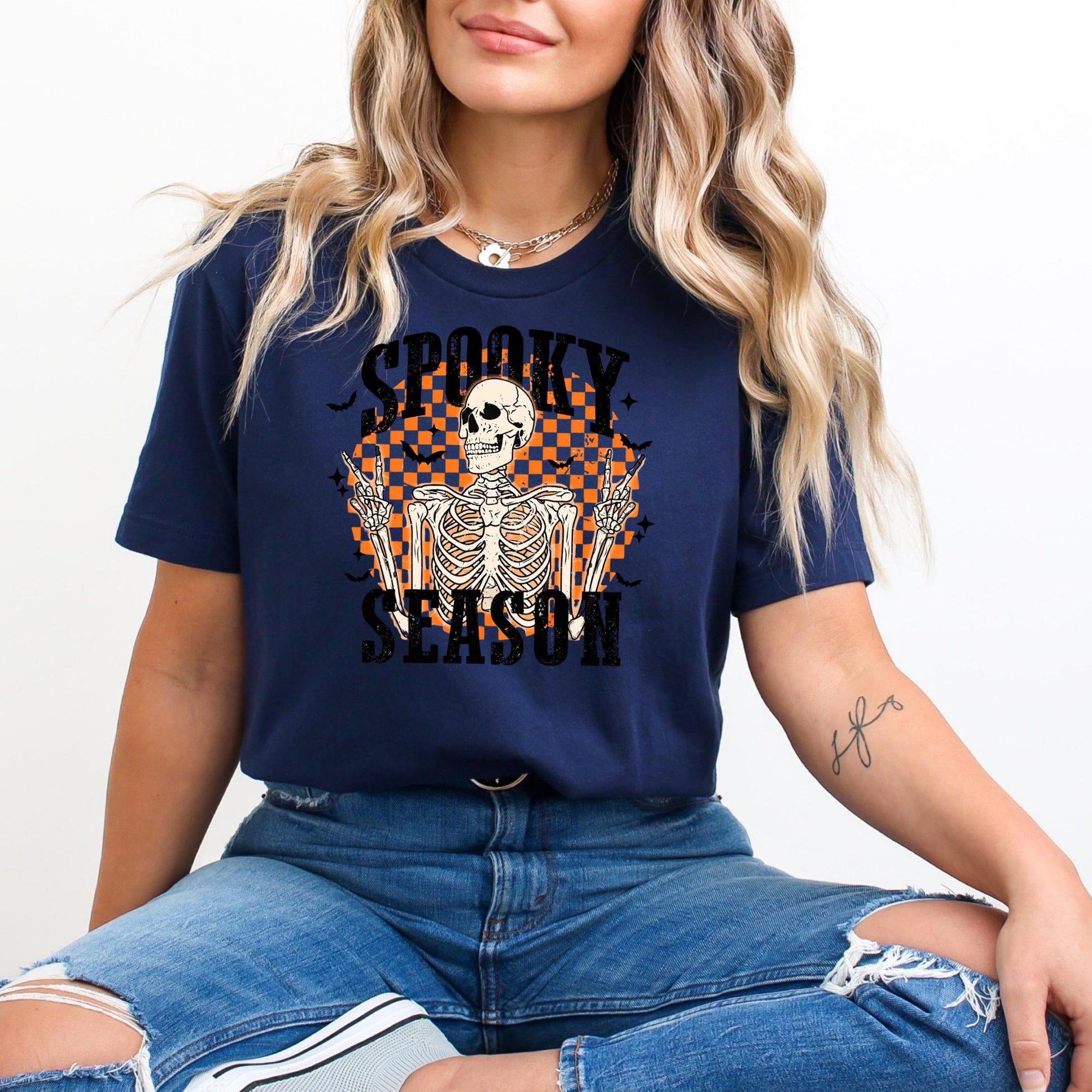 A woman wearing a navy blue t-shirt with a graphic of a skeleton and the text "SPOKY SEASON" is sitting on the floor.