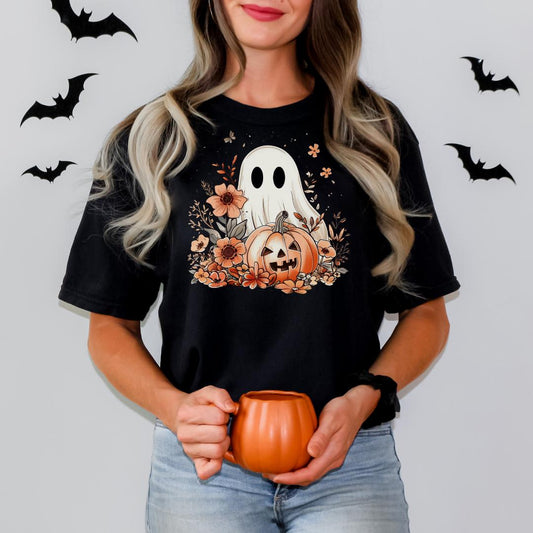 A woman wearing a black t-shirt with a Halloween-themed graphic of a ghost and a pumpkin, holding a small orange mug.
