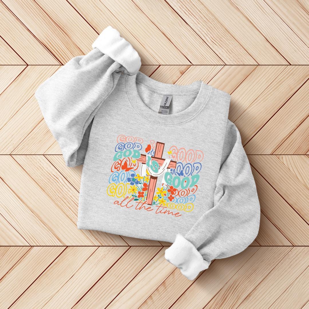 A gray sweatshirt with a colorful graphic design on the front, featuring a cross and the text "GOOD GOOD GOOD" in various colors.