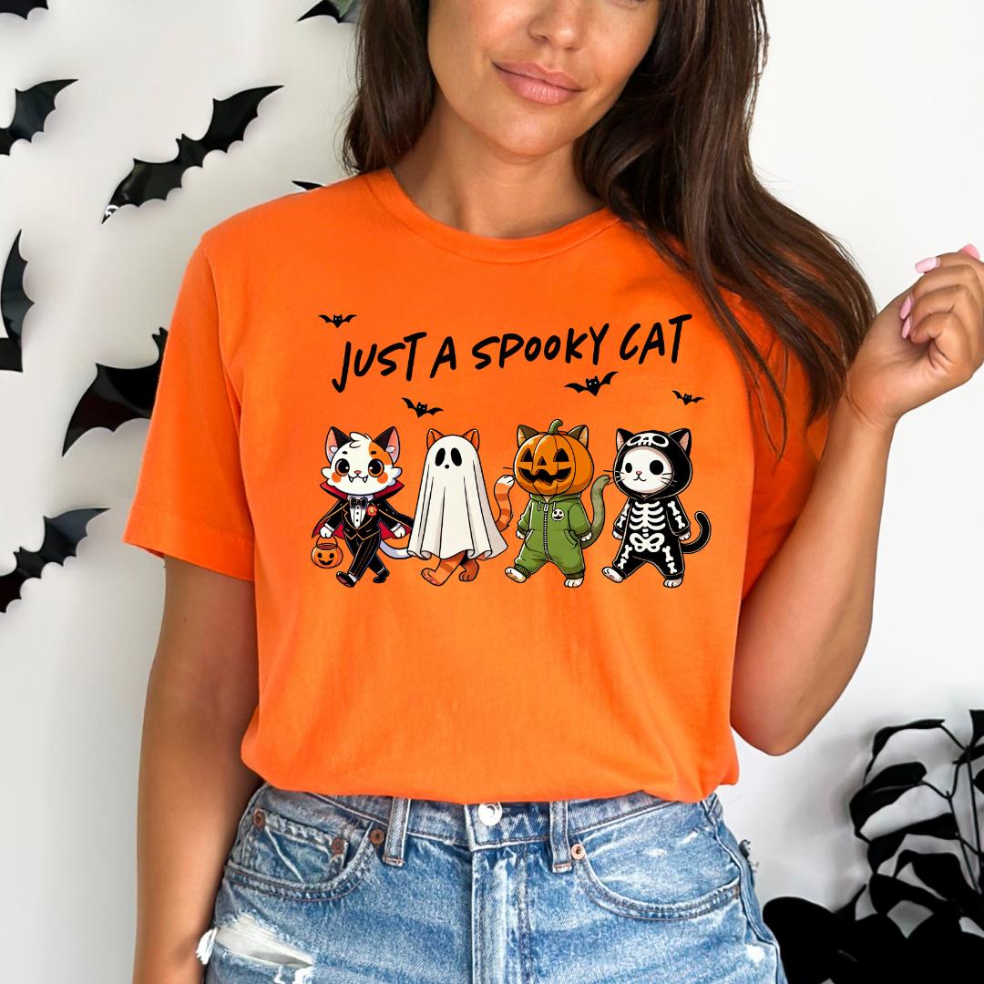 A woman wearing an orange t-shirt with a Halloween-themed graphic of four cartoon cats, including a ghost, skeleton, and jack-o-lantern.