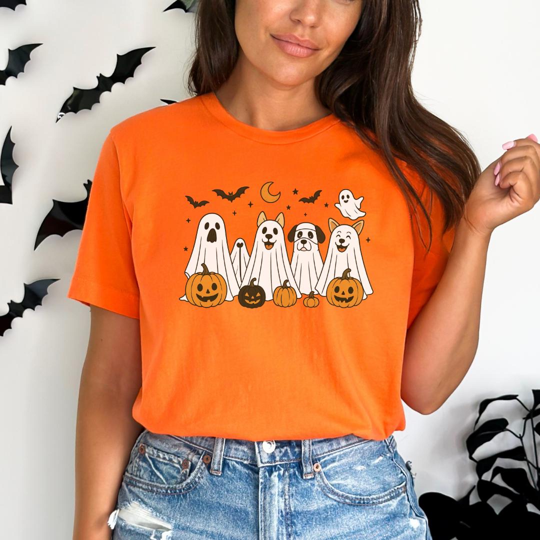 A woman wearing an orange t-shirt with a graphic of five ghost dogs and jack-o-lanterns.