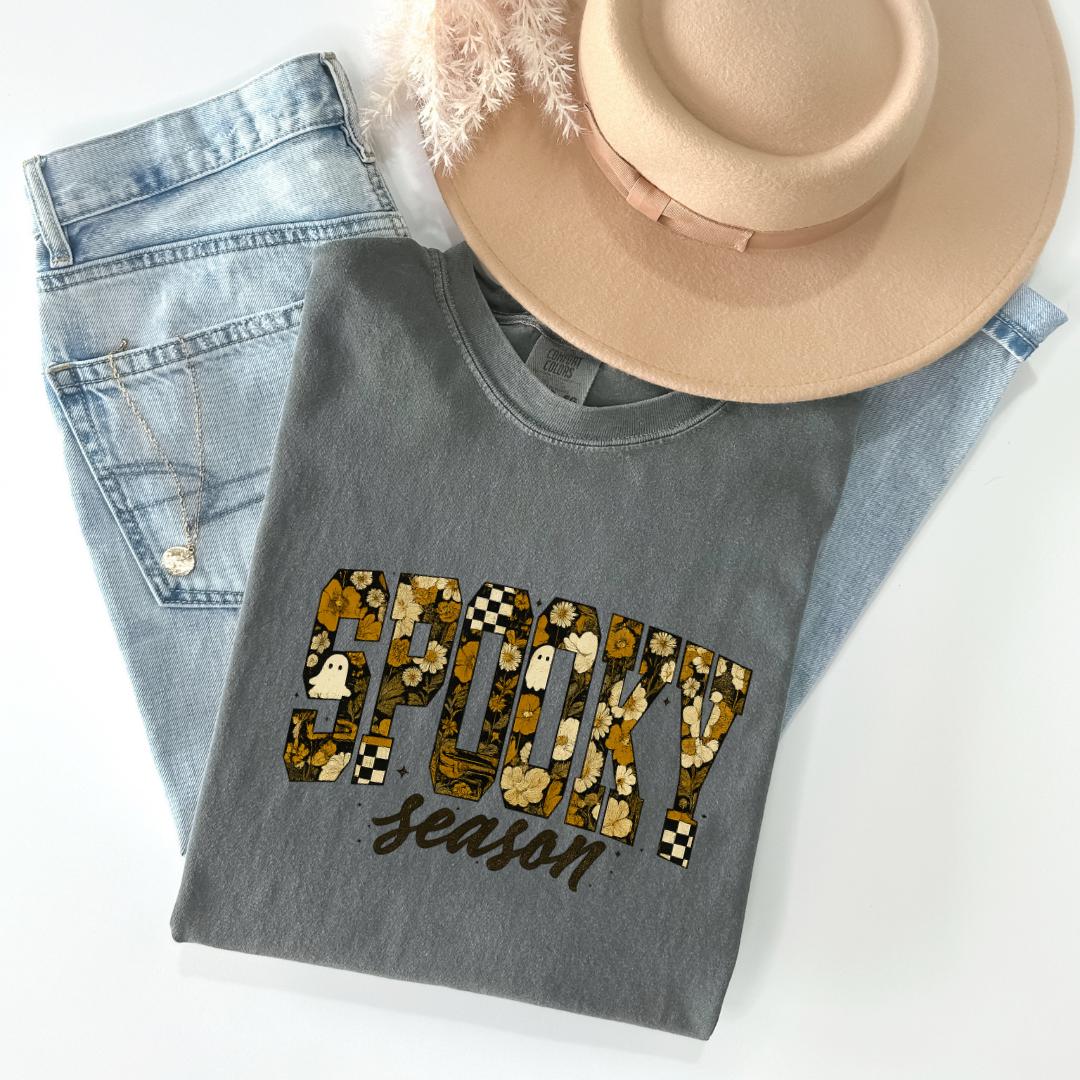 a gray t-shirt with the word "SPOKY season" printed on it, along with a beige hat and a pair of blue jeans.
