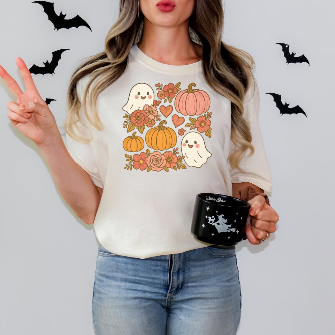 A woman wearing a white t-shirt with a graphic design of Halloween-themed ghost and pumpkin characters, holding a black mug with a star design.