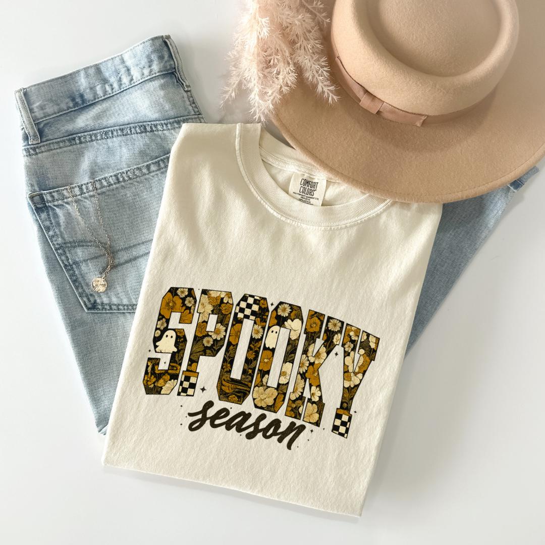 a white t-shirt with a floral print design, a pair of blue jeans, and a beige hat.
