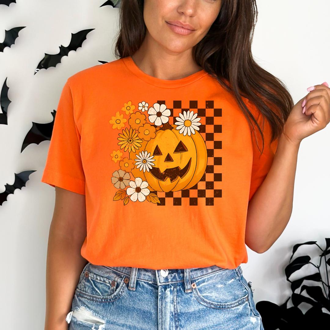 A woman wearing an orange t-shirt with a pumpkin and flower design, standing in front of a wall with bats.