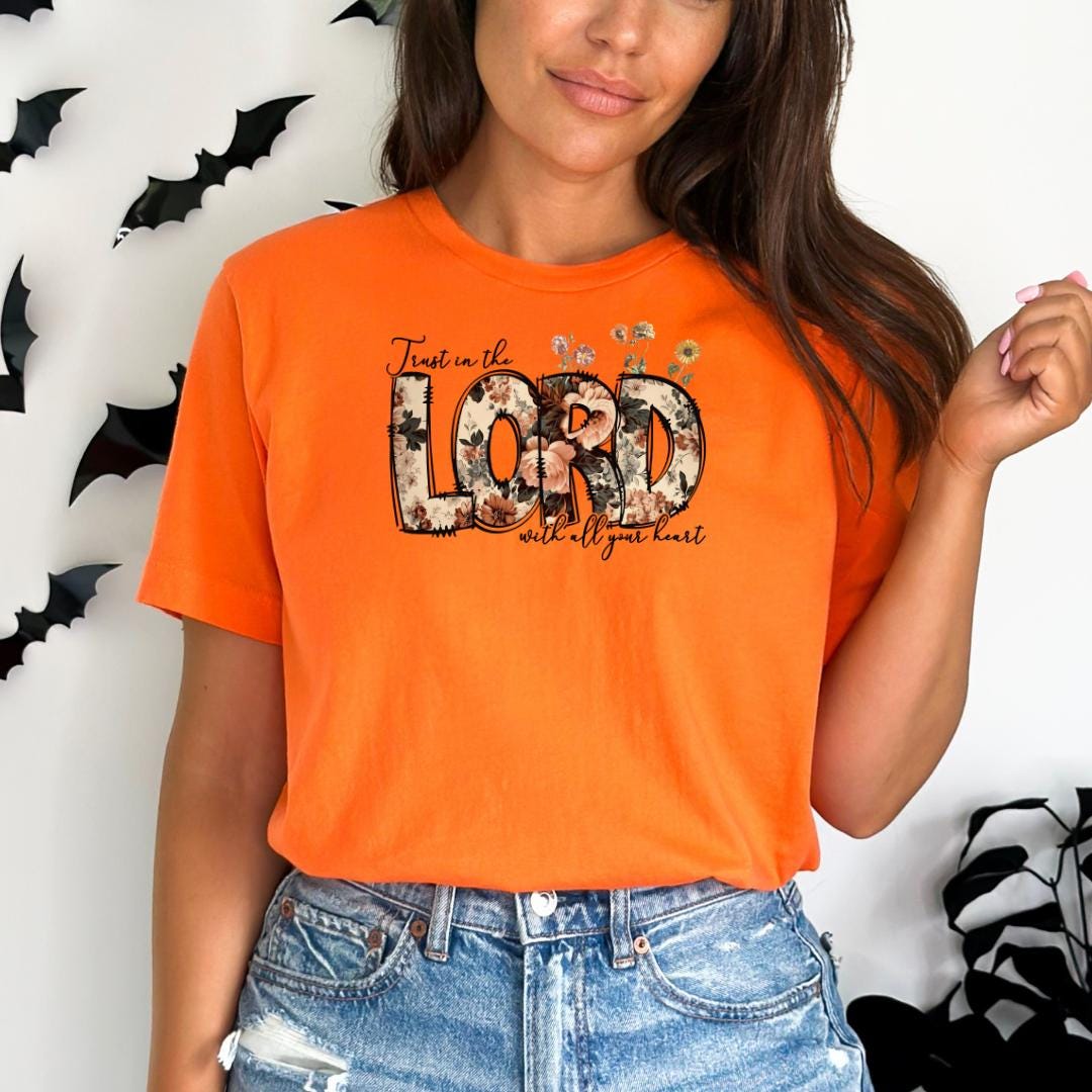 A woman wearing an orange t-shirt with the text "Trust in the LORD with all your heart" printed on it.