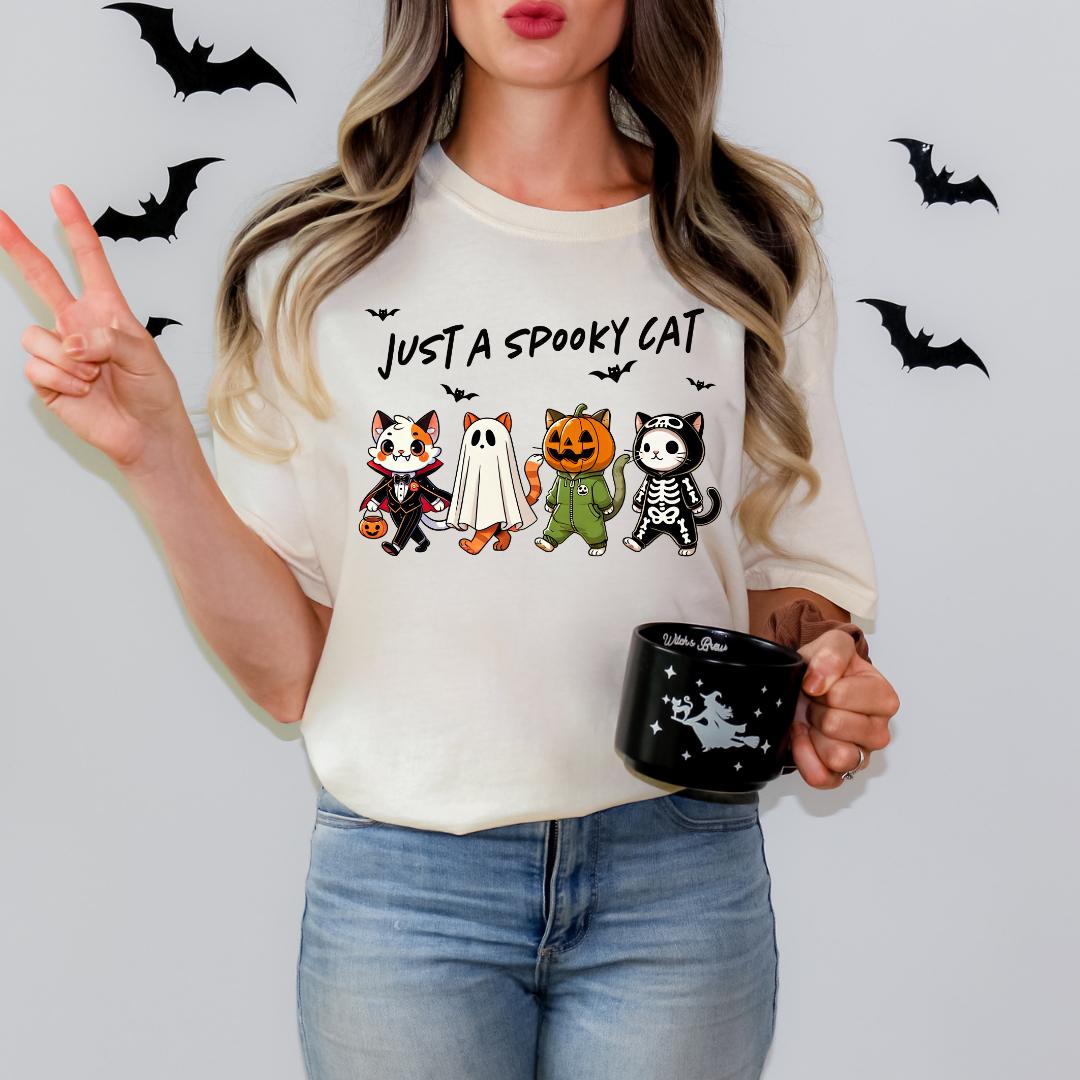 A woman wearing a white t-shirt with a graphic design of four cartoon cats and bats, holding a black mug with a star design.