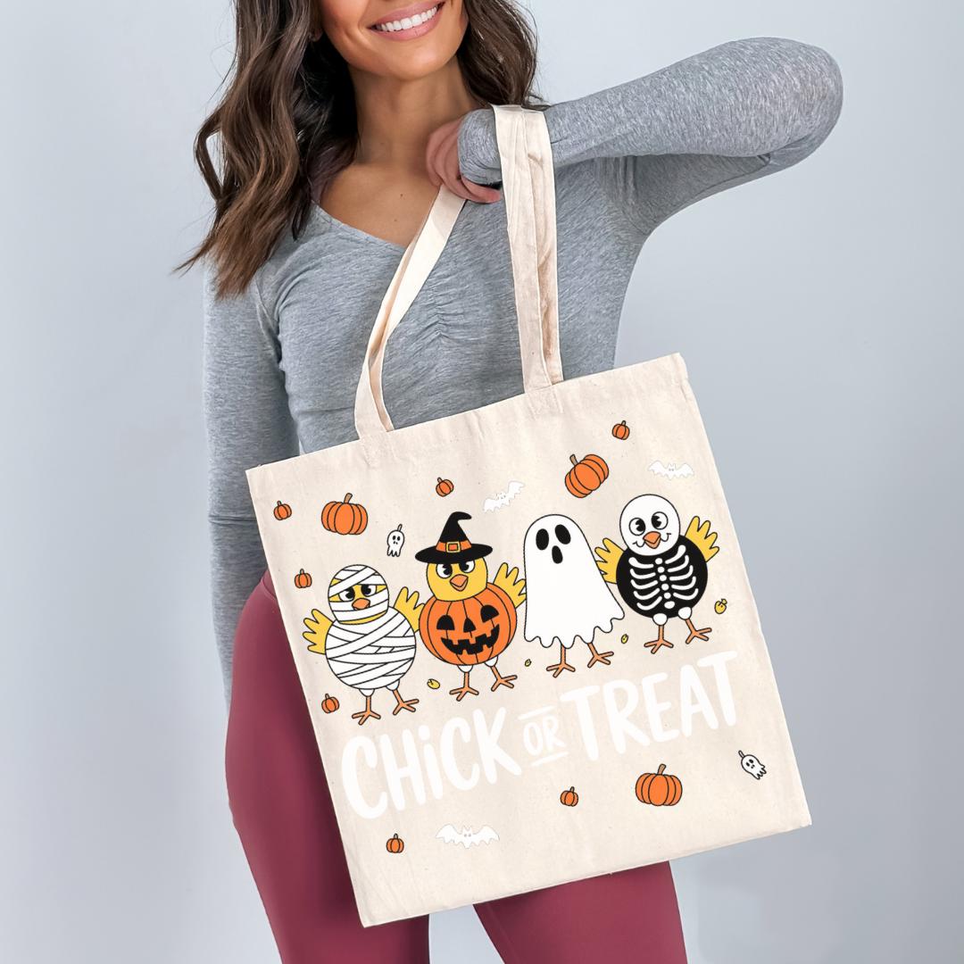 A woman is holding a large tote bag with a Halloween-themed design featuring cartoon birds and a pumpkin.