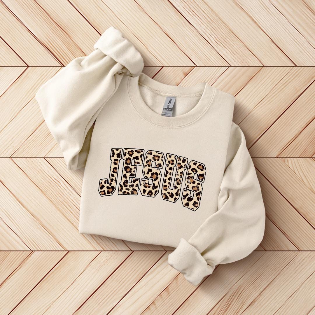 A white sweatshirt with the word "JESUS" printed on it in a leopard print design.
