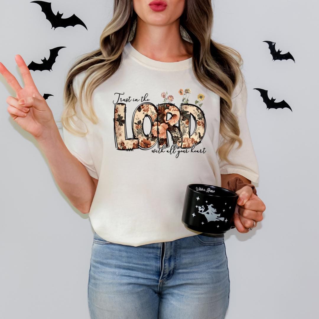 A woman wearing a white t-shirt with the text "Just in the LORD with all your heart" and holding a black mug with a white design.