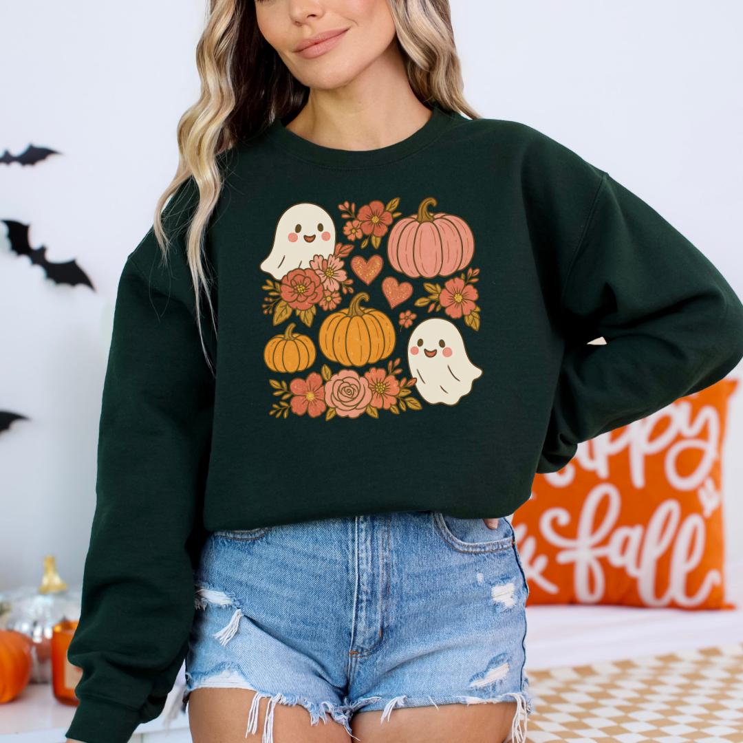 A woman wearing a green sweatshirt with a graphic design of Halloween-themed elements, including ghostly figures, pumpkins, and flowers.