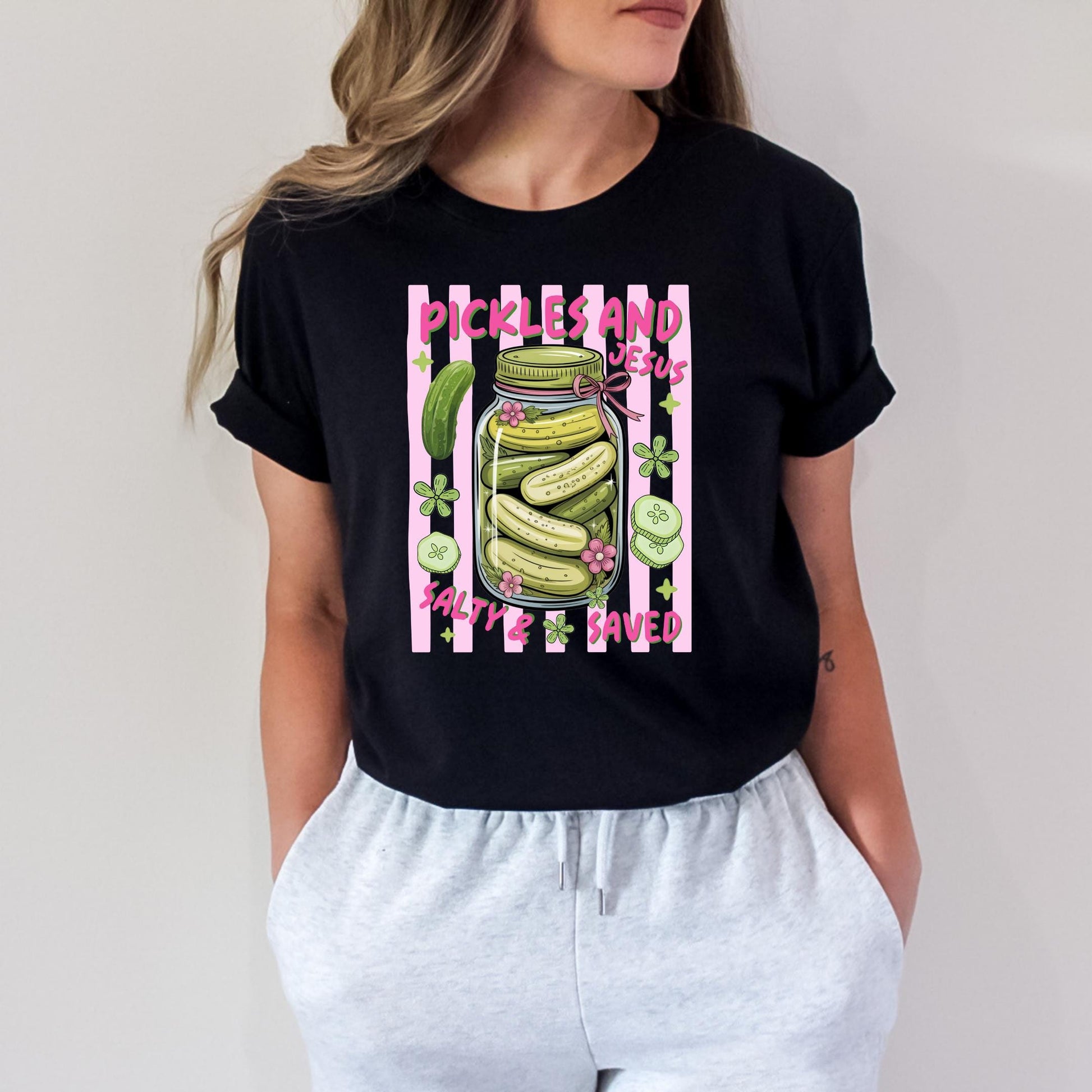 A woman wearing a black t-shirt with a graphic design of a jar filled with pickles and the text "Pickles and Joes Saved" printed on it.