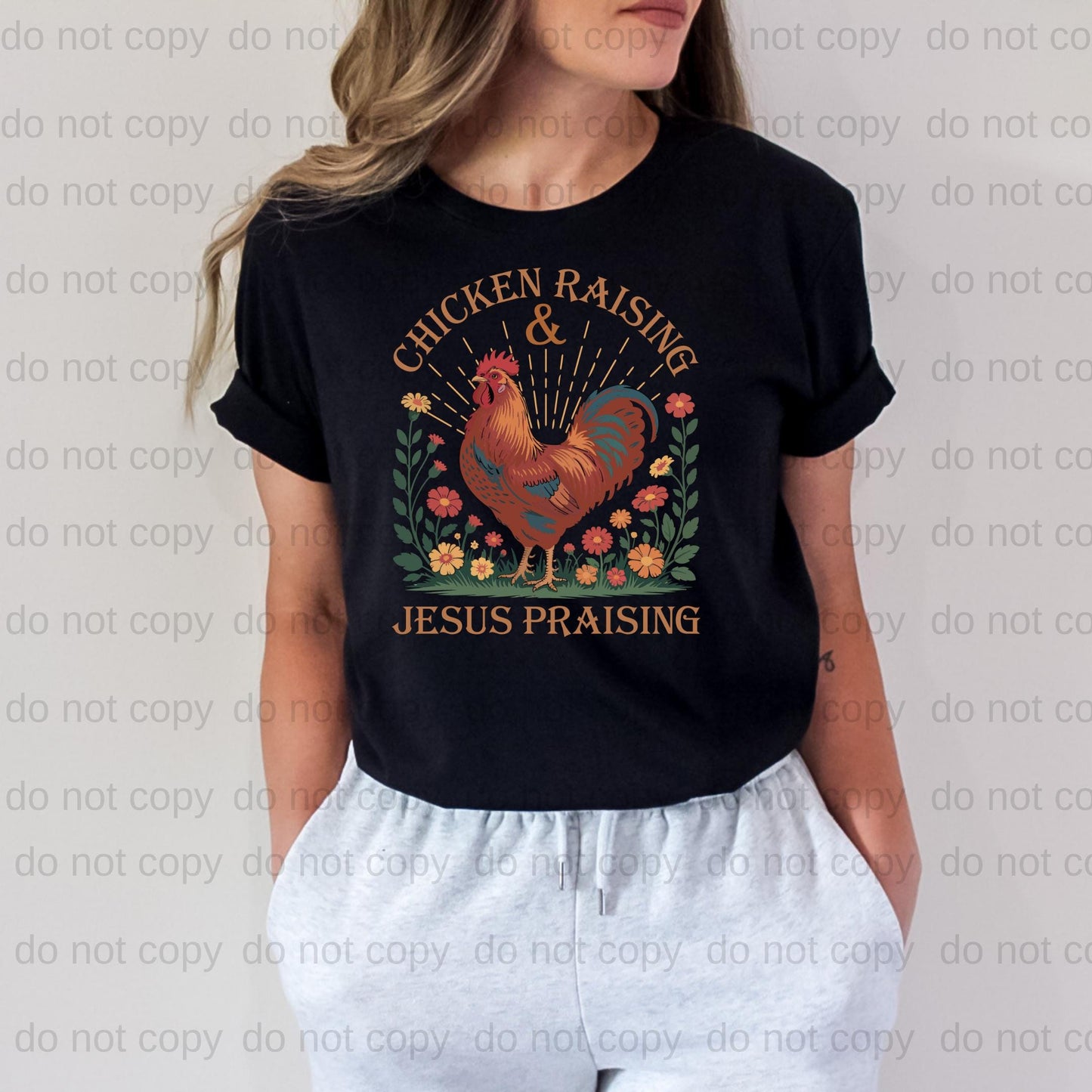 A woman wearing a black t-shirt with a graphic design of a rooster and the text "CHICKEN RAISING & JESUS PRASING" printed on it.