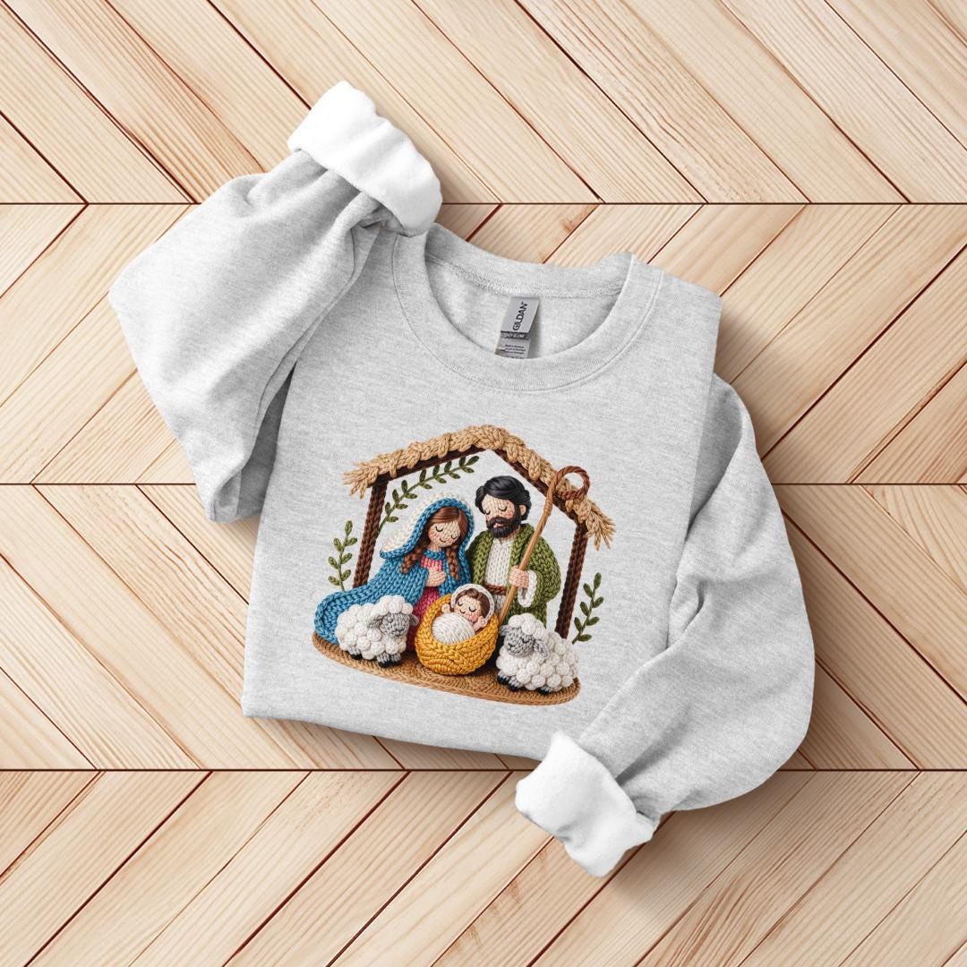 A gray sweatshirt with a detailed embroidered image of the Holy Family in a nativity scene, including the mother, father, baby Jesus, and sheep.