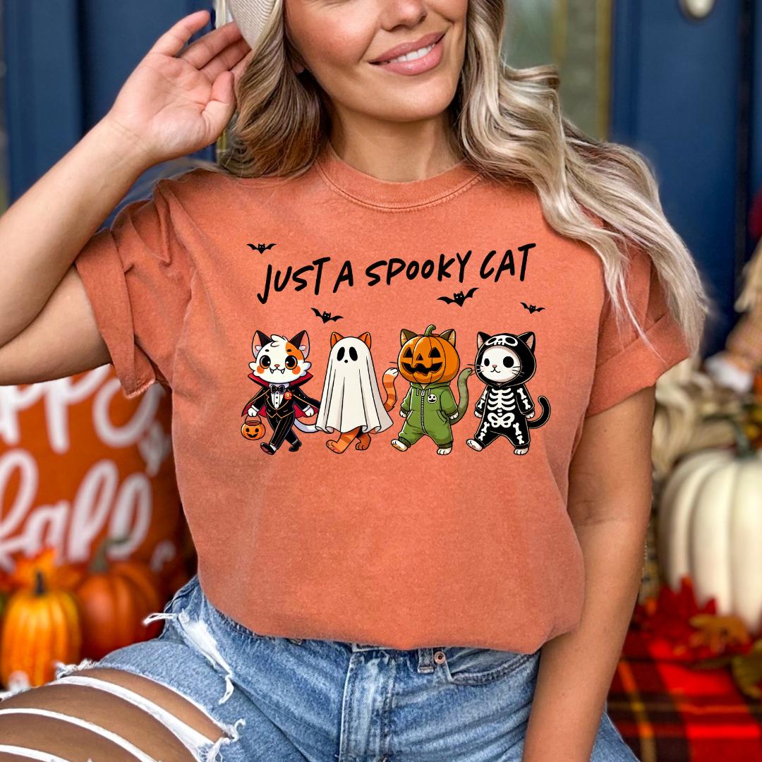 A woman wearing a t-shirt with a Halloween-themed graphic of four cartoon cats, including a skeleton cat, a ghost, a skeleton cat, and a cat dressed in a skeleton costume.