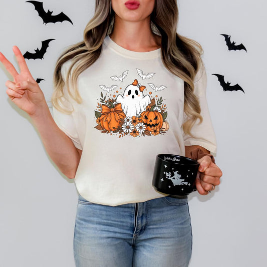 A woman wearing a white t-shirt with a graphic of a ghost and bats, holding a black mug with a white design.