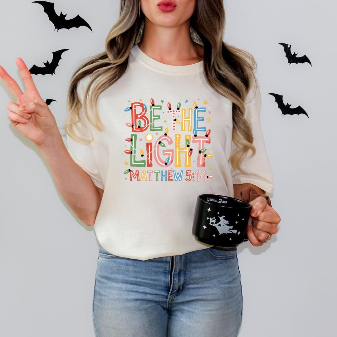 A woman wearing a white t-shirt with a colorful design and holding a black mug with a star and a bat graphic.