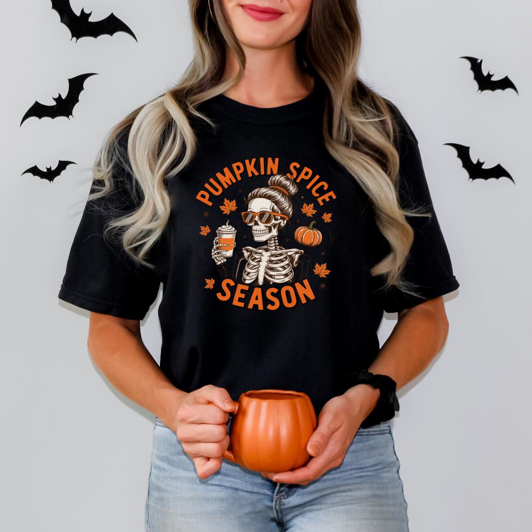 A woman wearing a black t-shirt with a pumpkin spice season graphic and holding a pumpkin-shaped mug.