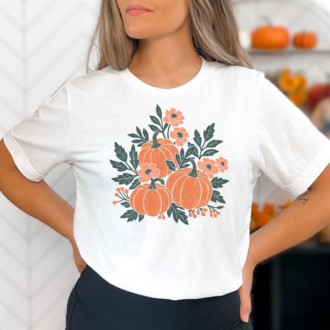 A woman wearing a white t-shirt with a graphic design of orange pumpkins and green leaves.