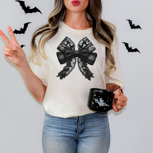 A woman with long, wavy hair is standing against a white background, holding a black mug with a bow design on it. There are black bats decorating the background.